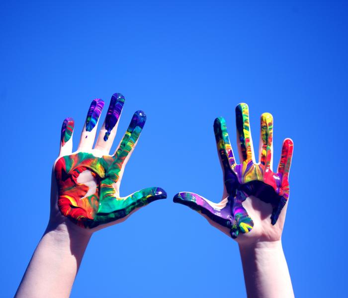 Two hands painted colorful reaching for the blue sky