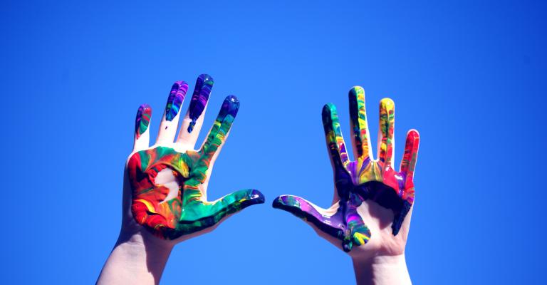 Two hands painted colorful reaching for the blue sky