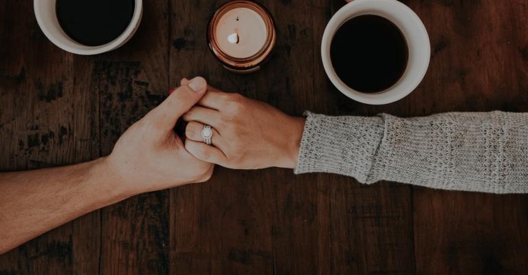 Two hands holding each other next to coffee cups